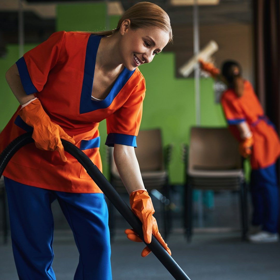 Nettoyage de bureaux Deux femmes en uniforme nettoient une pièce, l'une passe l'aspirateur et l'autre frotte.